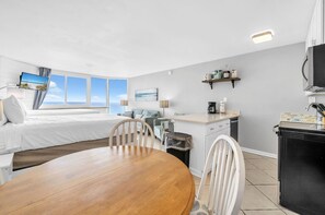 A hotel room with a bed, a dining table, a kitchen area, and a view of the sea. - Top of the Gulf 813 (Panama City Beach)