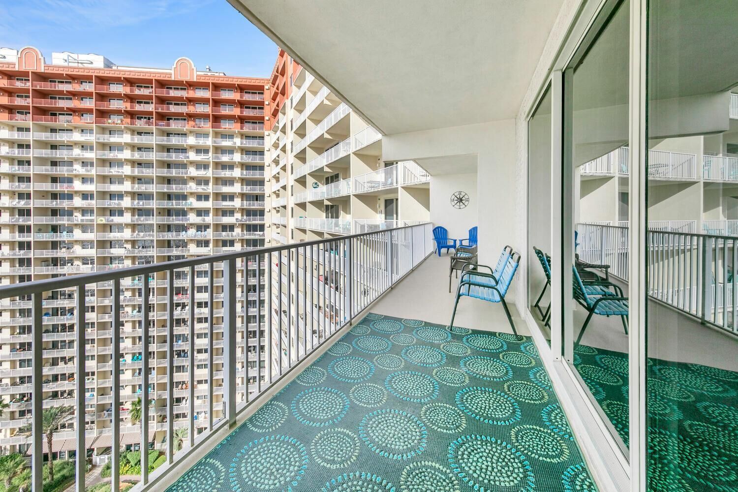 A balcony with a patterned floor, two blue chairs, and a table.