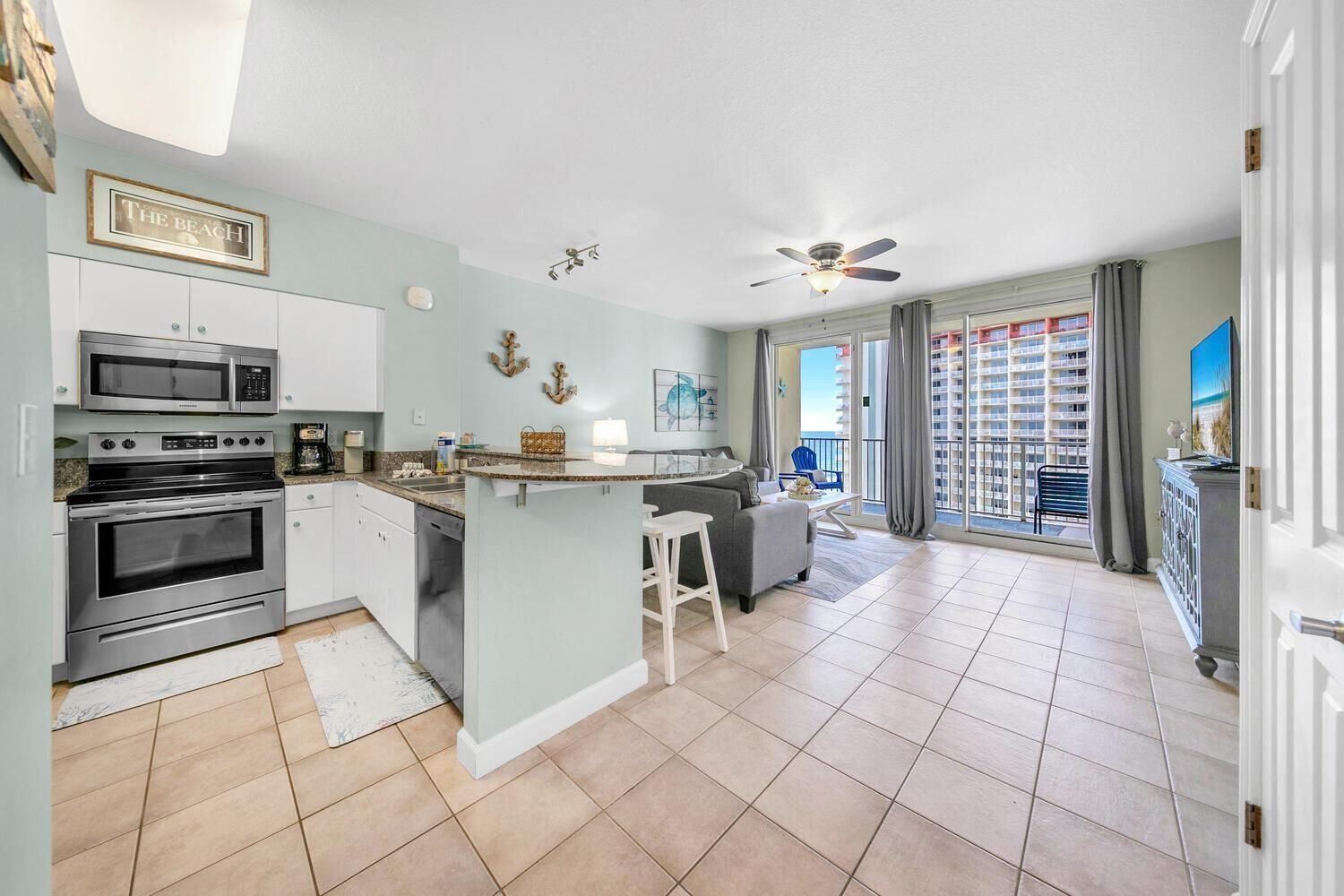 A modern kitchen with a central island, stainless steel appliances, and a view to a balcony with a cityscape.
