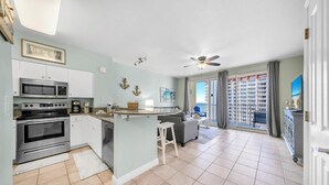 A modern kitchen with a central island, stainless steel appliances, and a view to a balcony with a cityscape. - Shores of Panama 1523 (Panama City Beach)