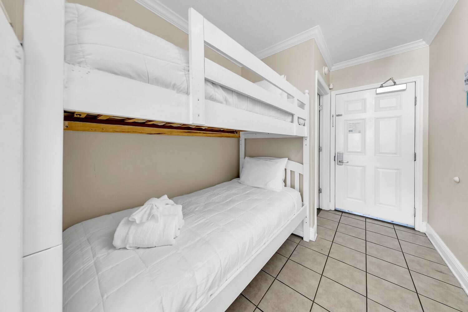 A room with bunk beds, a white door, and a tiled floor.