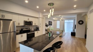 A modern kitchen with stainless steel appliances, a black countertop, and a central island with bar stools. - Escape to our chic casita where modern comfort meets serene surroundings.  (Cambridge)