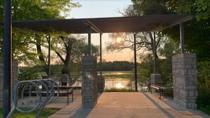 A covered outdoor area with benches and a view of a lake at sunset. - Escape to our chic casita where modern comfort meets serene surroundings.  (Cambridge)