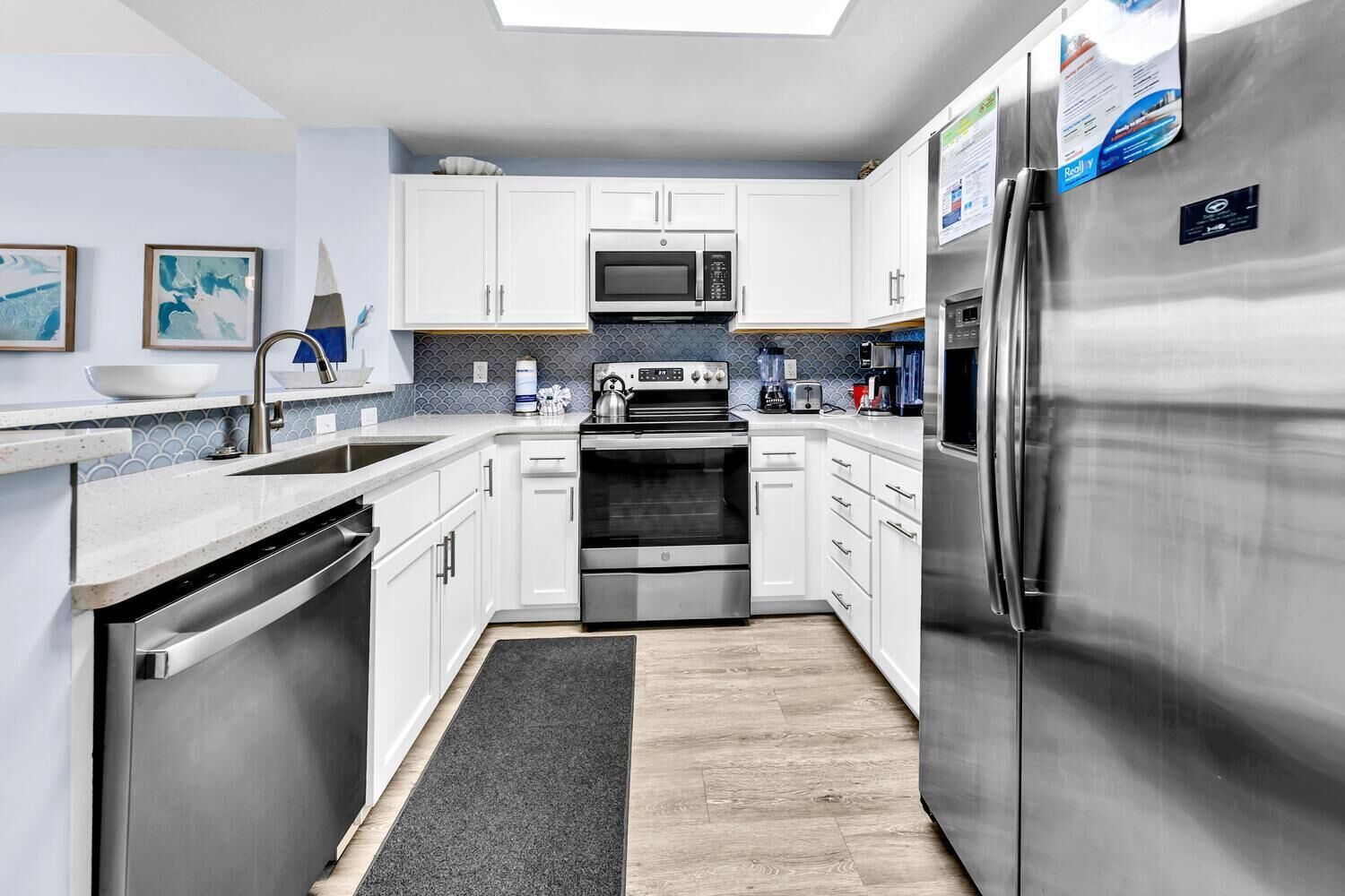Una cocina moderna con armarios blancos, electrodomésticos de acero inoxidable, microondas, horno y refrigerador.