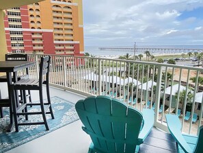 A balcony with a view of the beach, a dining table, chairs, and a blue patterned rug. - Calypso 3-406 - Paradise by the Pier (Panama City Beach)