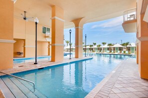 A swimming pool area with a tiled deck, a ceiling fan, and a view of the resort buildings in the background. - Calypso 3-406 - Paradise by the Pier (Panama City Beach)