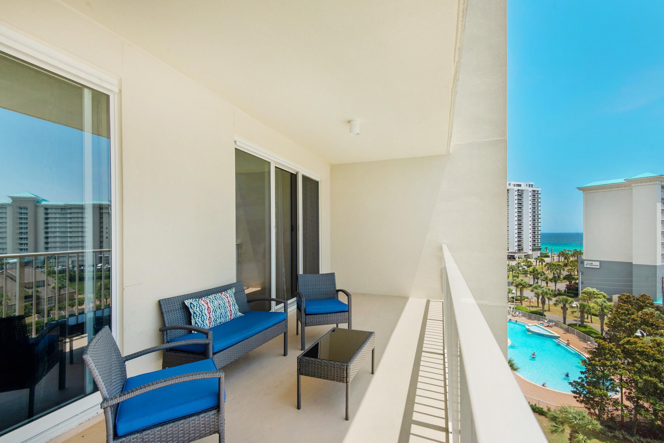 A balcony with wicker furniture, a glass door, and a view of a swimming pool and buildings.