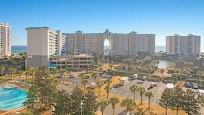 A hotel with a central archway, multiple floors, and a parking lot with palm trees. - Ariel Dunes II 703 (Miramar Beach)