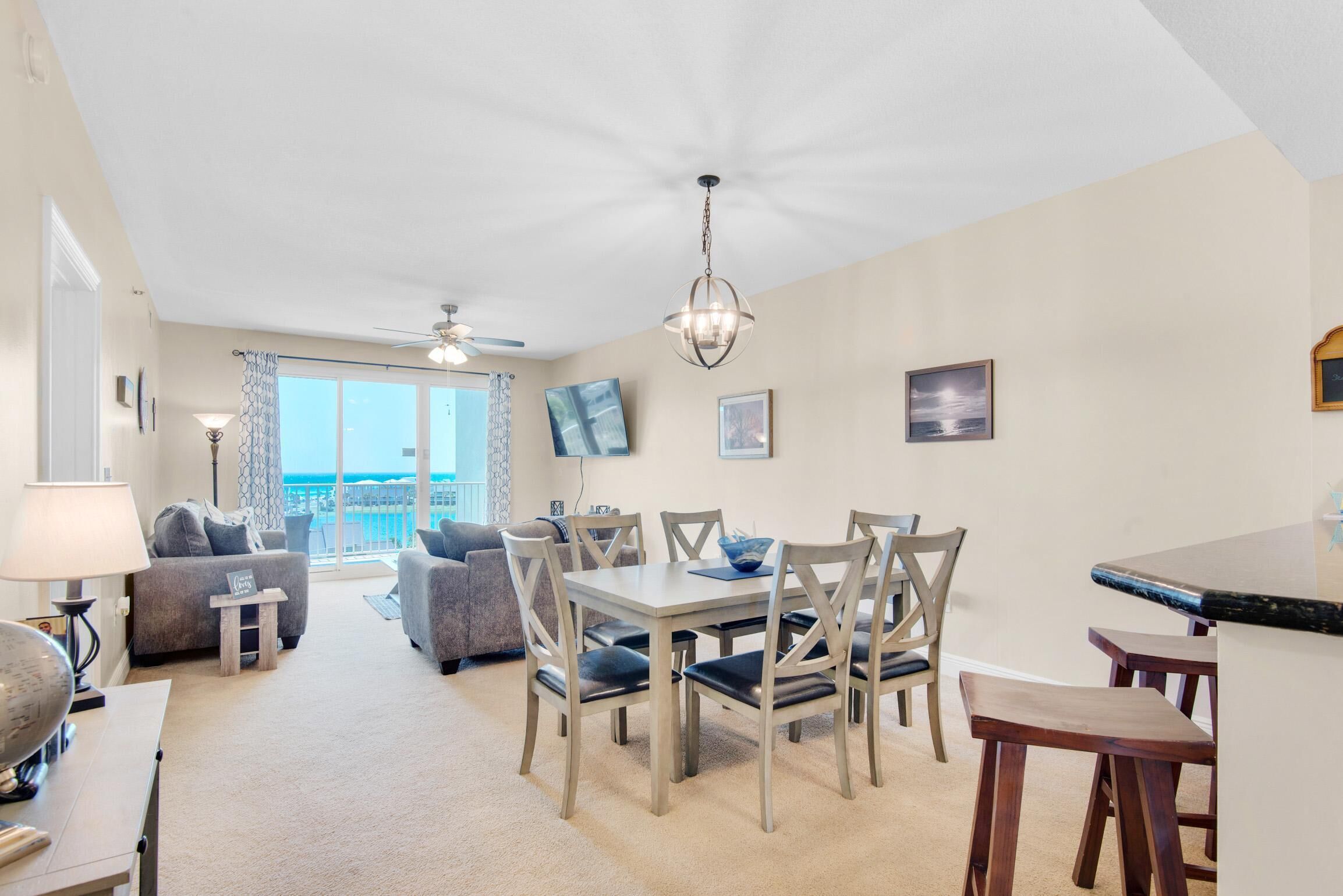 A dining area with a table and chairs, a ceiling fan, and a view of the ocean through large windows.