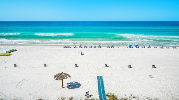 Ein Strand mit Liegestühlen und Sonnenschirmen, ein Reetdach-Sonnenschirm und ein blaues Surfbrett.
