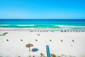 Ein Strand mit Liegestühlen und Sonnenschirmen, ein Reetdach-Sonnenschirm und ein blaues Surfbrett.