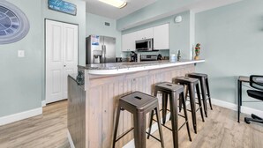 A modern kitchen with a central island, bar stools, and a refrigerator. - Shores of Panama 830 (Panama City Beach)