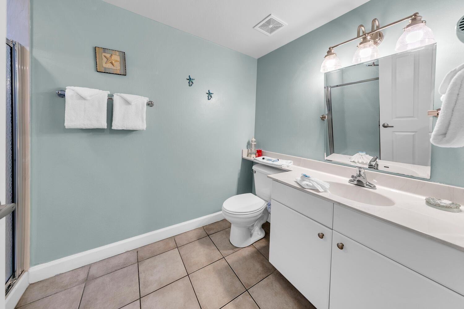 A bathroom with a toilet, sink, and mirror. There are two towels hanging on the wall.