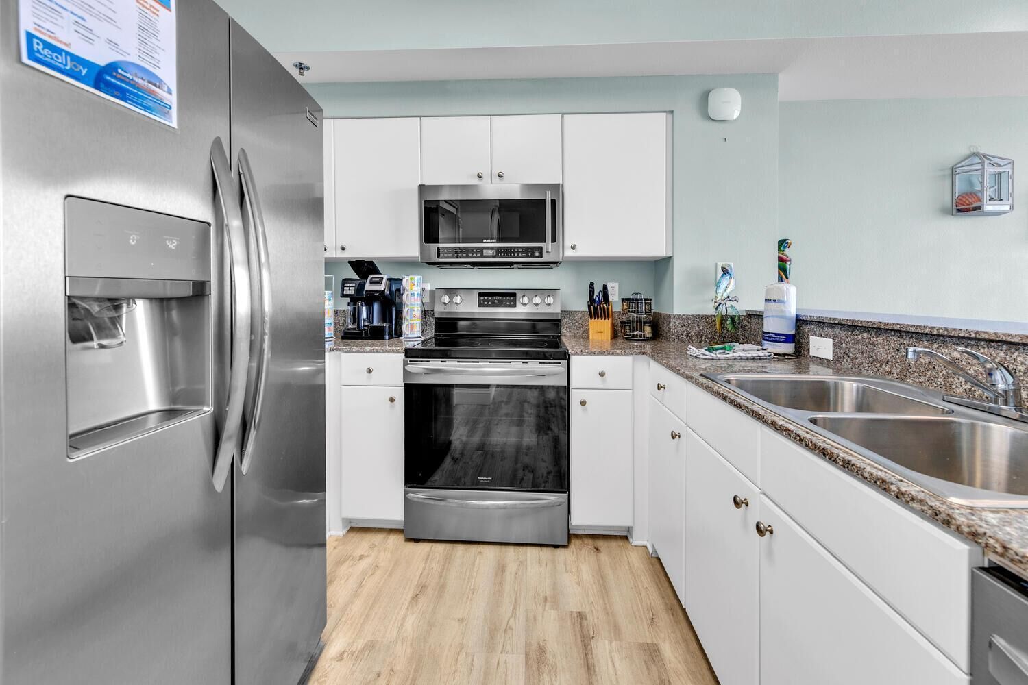 A modern kitchen with stainless steel appliances, white cabinetry, a granite countertop, and a double sink.