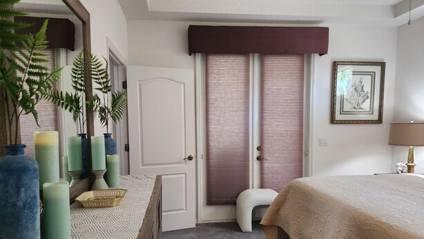 Ein Schlafzimmer mit einem Bett, einem Schminktisch, einem Spiegel, einem Fenster mit Jalousien und einem gerahmten Bild an der Wand.