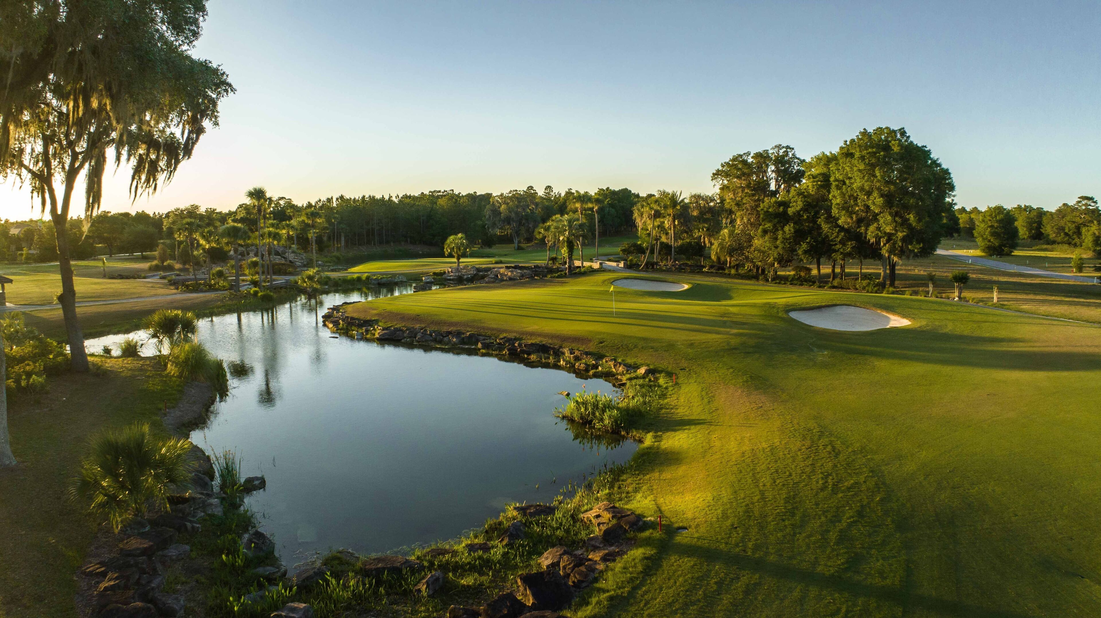 Un campo de golf con un estanque, árboles y cielo despejado.