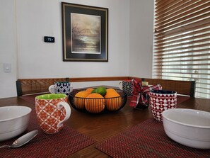 A dining table with bowls, a fruit bowl, and patterned mugs. There is a framed picture on the wall and a thermostat. - Lovely Home Near Rainbow Springs, World Equestrian Center, and Juliette Falls! (Dunnellon)