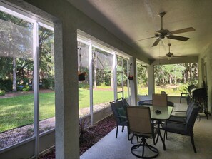 A covered patio with a table and chairs, large windows, and a ceiling fan. - Lovely Home Near Rainbow Springs, World Equestrian Center, and Juliette Falls! (Dunnellon)