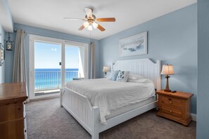 A bedroom with a bed, nightstands, a ceiling fan, a window with a view of the ocean, and a door leading to a balcony. - Laketown Wharf 1626 (Panama City Beach)