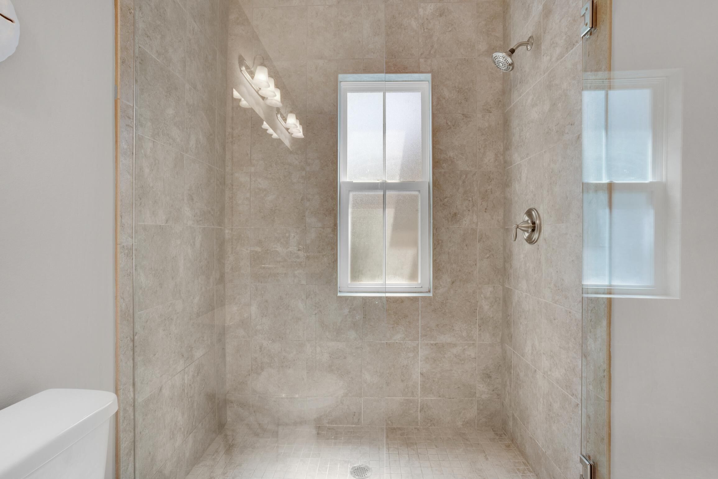 A modern bathroom with a glass shower enclosure, a toilet, and a window.