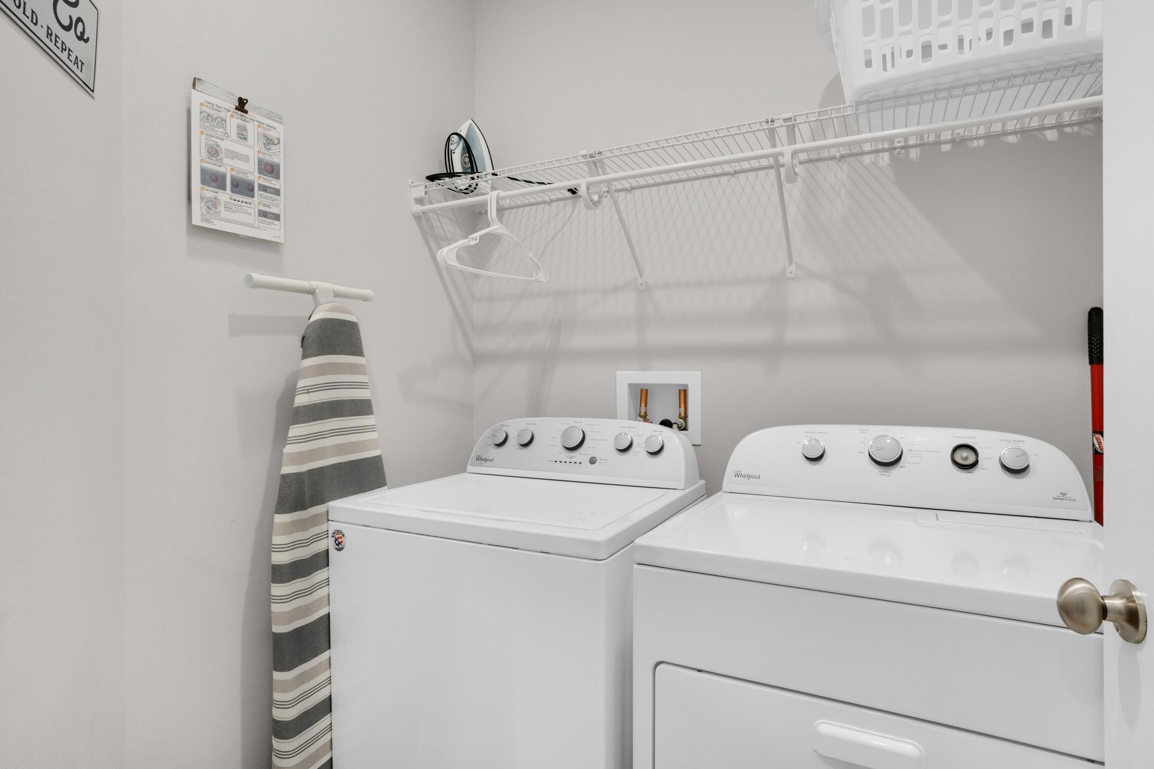 A laundry room with two white washers and dryers, a drying rack, and a striped towel hanging on a rack.