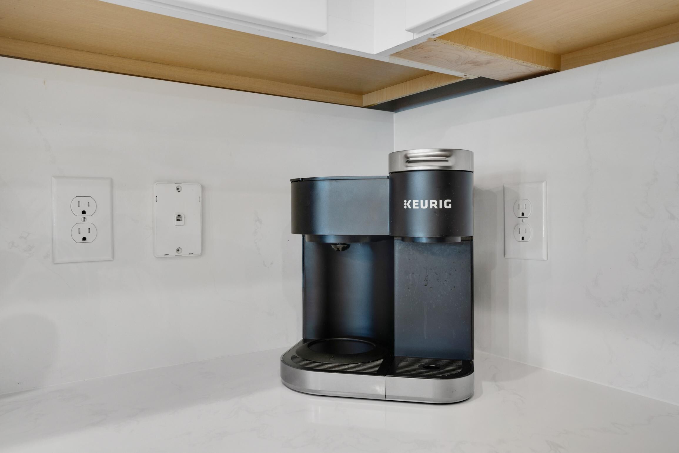 A modern coffee machine with a sleek design, placed on a white countertop in a kitchen with marble backsplash and wooden ceiling beams.