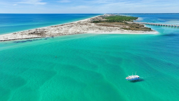 An aerial view of a coastal area with clear turquoise waters, a boat, and a pier extending into the sea.