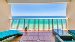 A balcony with a view of the ocean, a bird on the railing, and two green cushioned chairs.