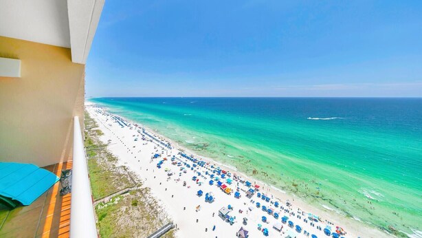 A beach view from a balcony with a clear sky, a sandy beach, and a calm sea.
