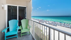 A balcony with two green Adirondack chairs, a view of a beach with numerous umbrellas and people, and a clear blue sky. - Tidewater 302 (Panama City Beach)