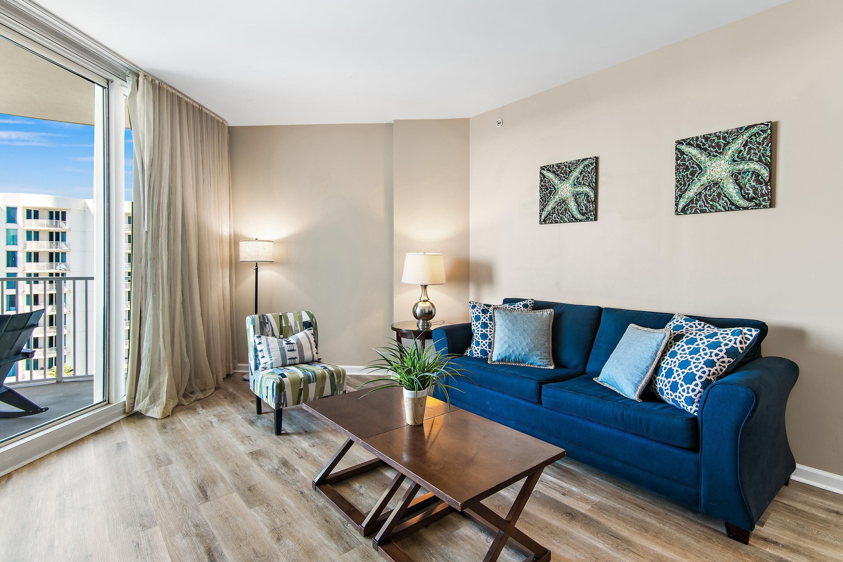 Ein modernes Wohnzimmer mit einem blauen Sofa, einem Holztisch und Blick auf die Stadt durch große Fenster.