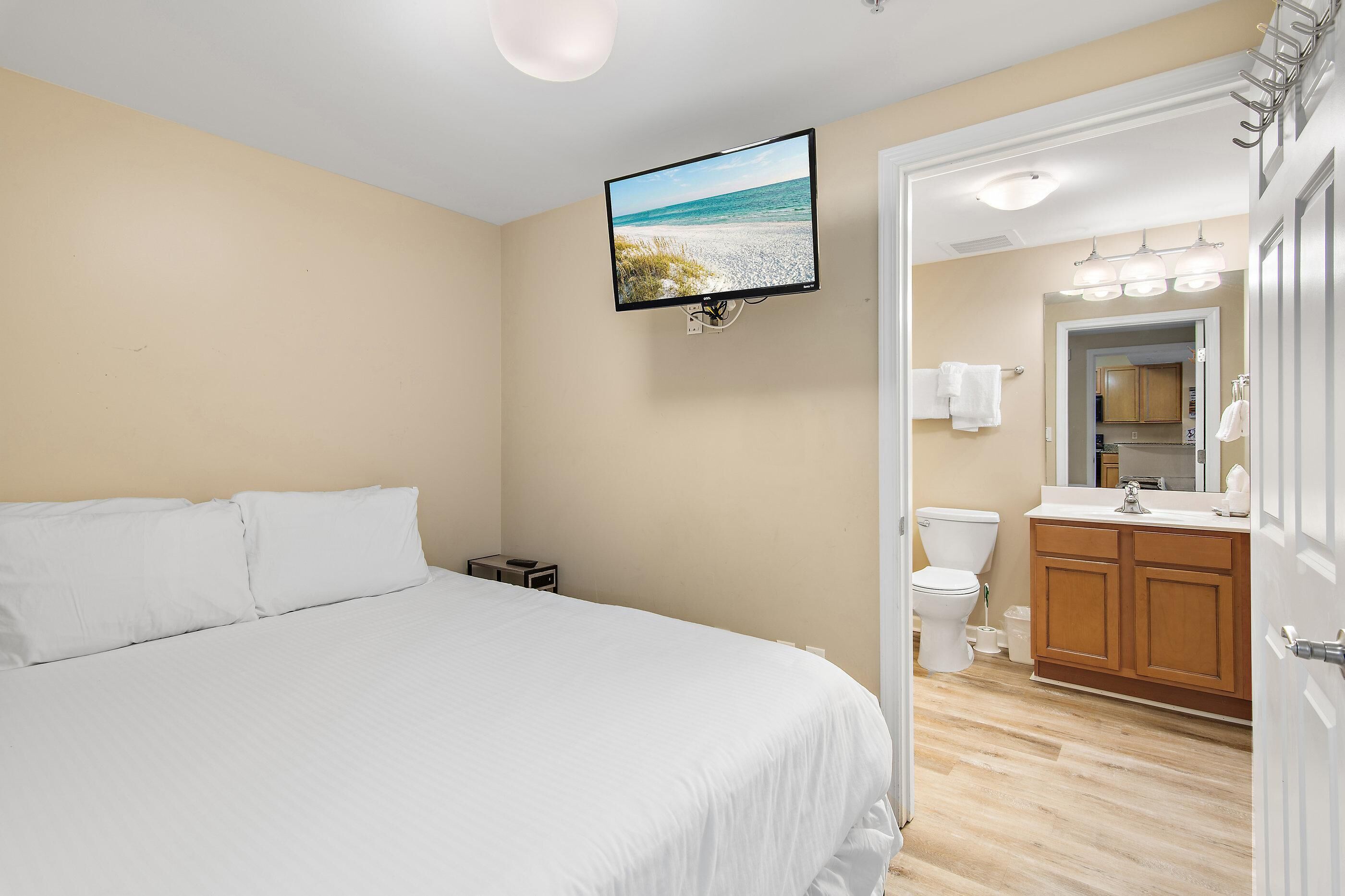A bedroom with a bed, a TV mounted on the wall, and a view of the bathroom through an open door.