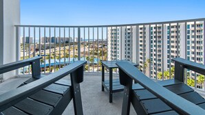 A balcony with two wooden tables and chairs, overlooking a cityscape with high-rise buildings and a parking area. - Palms Resort #11007 Jr 2BR (Destin)