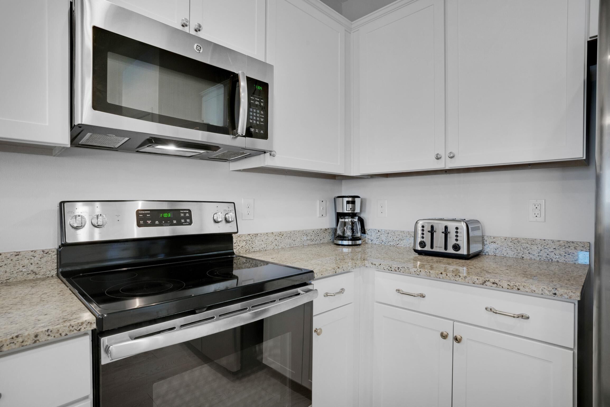 A kitchen with white cabinets, a stainless steel microwave, a stove, a toaster, and a coffee maker.