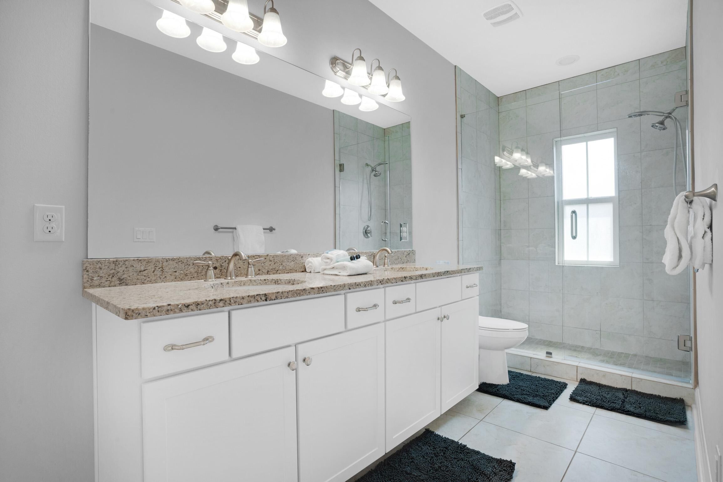 Een moderne badkamer met een grote spiegel, twee wastafels, toilet en een douchecabine met glazen wanden.