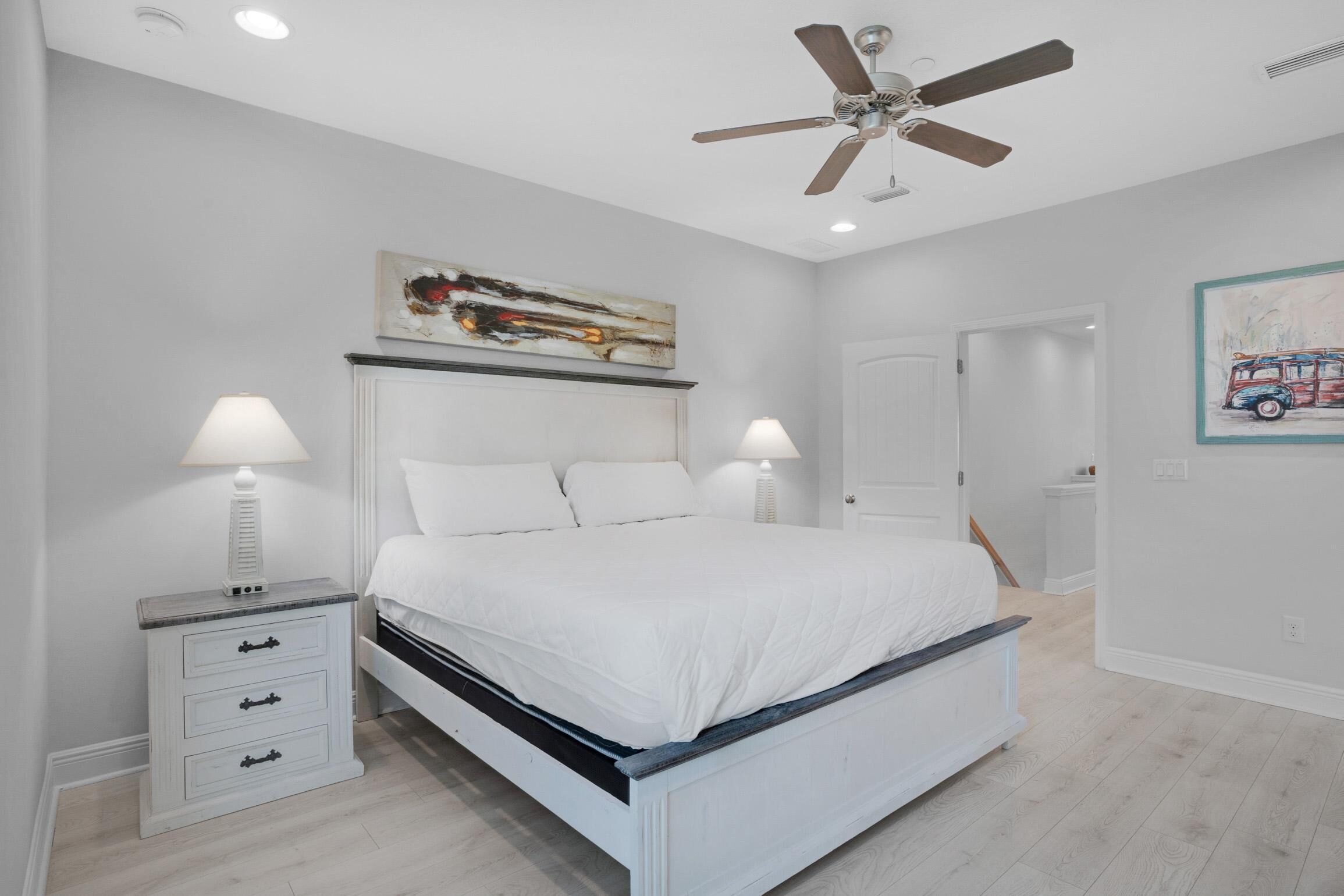 A bedroom with a bed, two bedside tables, a ceiling fan, and artwork on the walls.