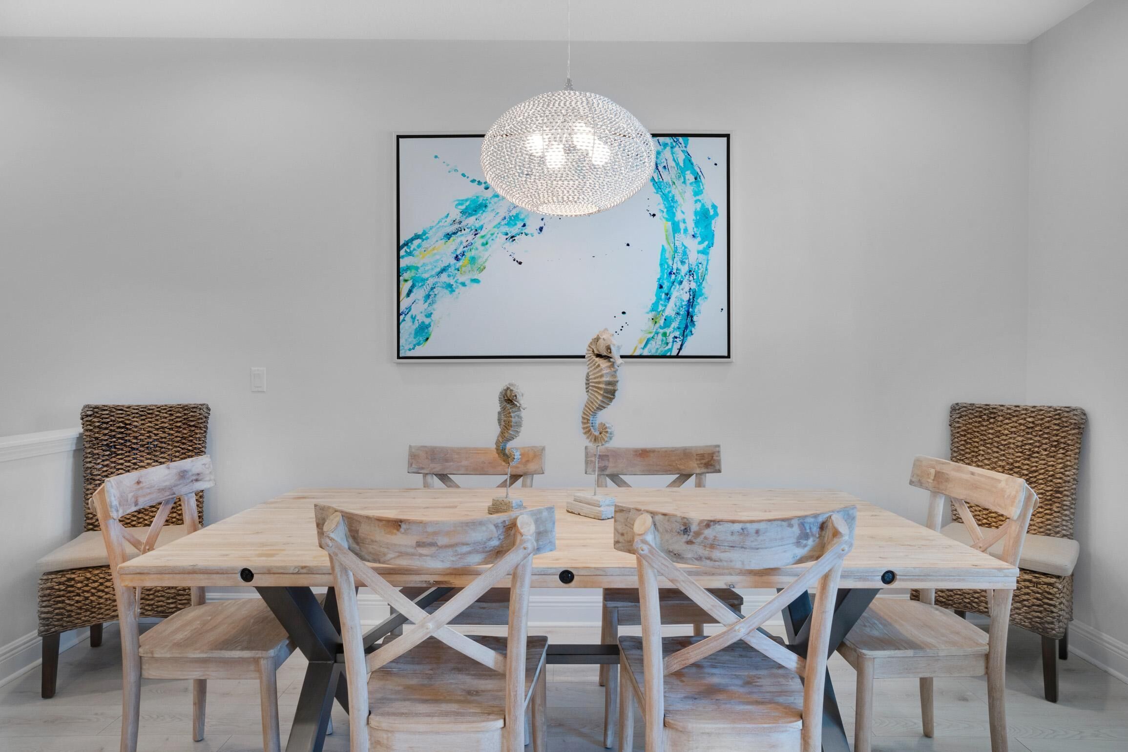 A dining area with a wooden table and chairs, a chandelier, and a large abstract painting on the wall.