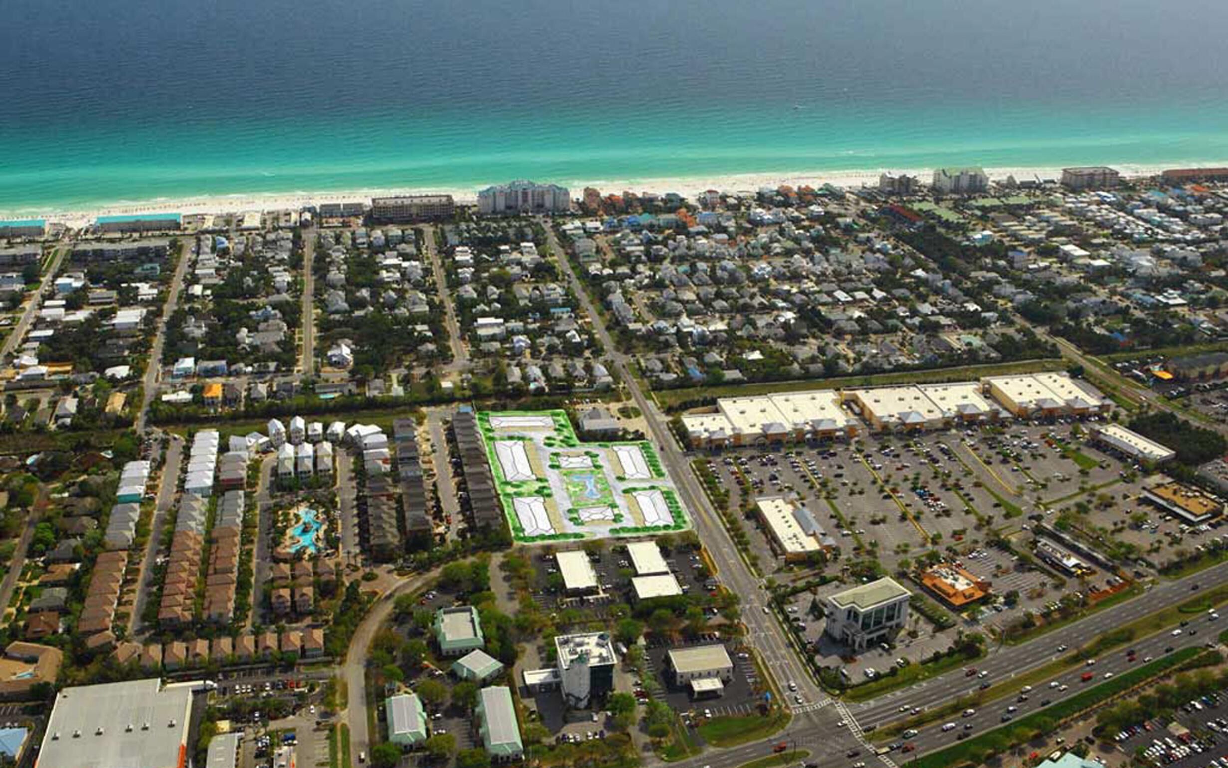 An aerial view of a coastal city with a dense residential area, a large commercial zone, and a beach in the background.
