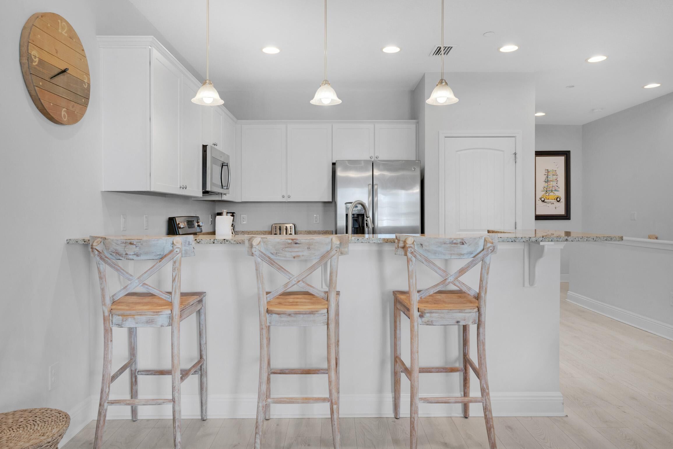 Une cuisine moderne avec des meubles blancs, un réfrigérateur en acier inoxydable et un îlot central en bois doté de tabourets de bar.