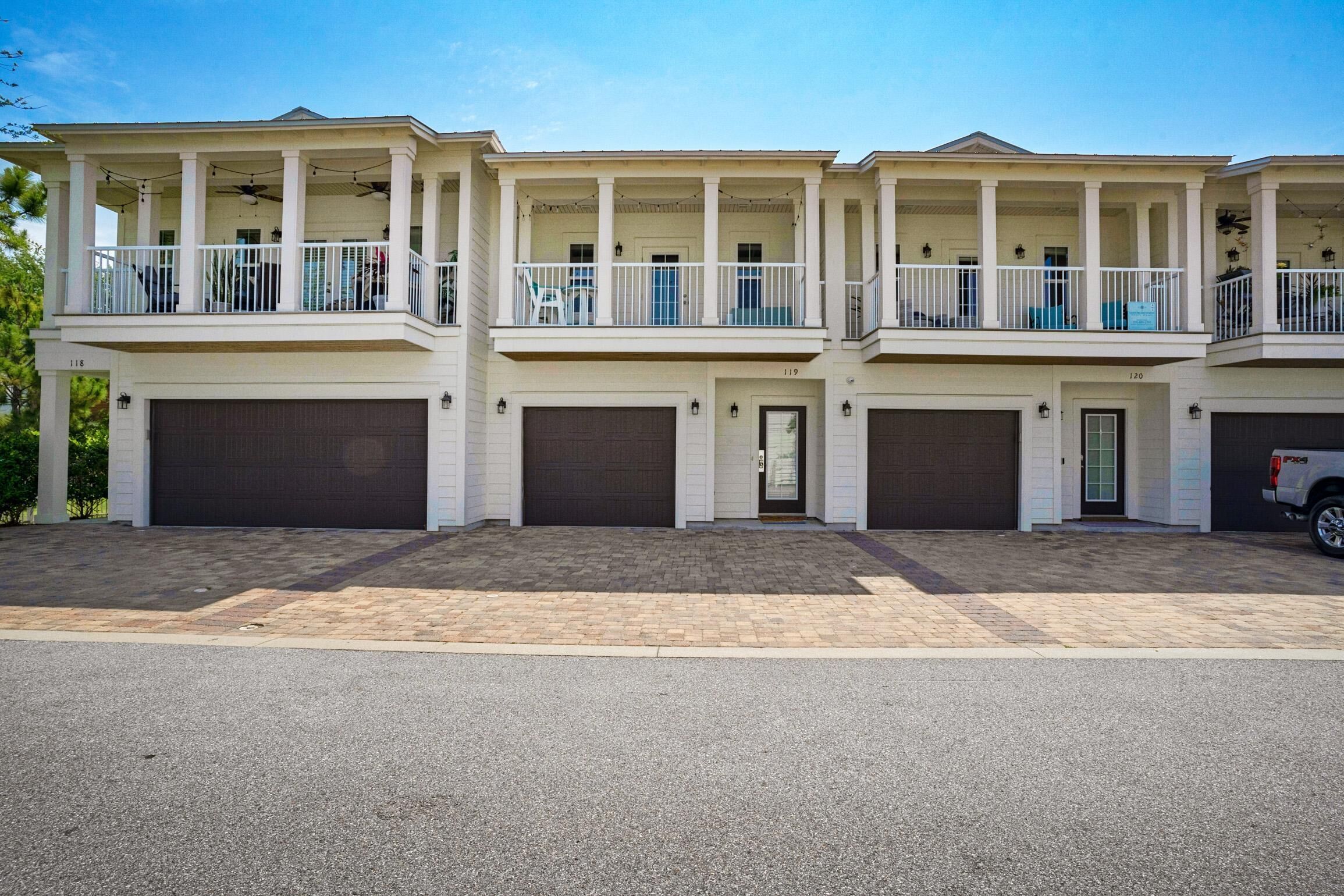 A two-story residential building with a covered balcony on the upper floor, a garage on the ground floor, and a clear sky.