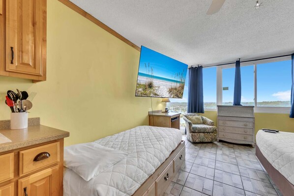 A room with a bed, a chair, a dresser, and a painting of a beach scene. - Top of the Gulf 822 (Panama City Beach)
