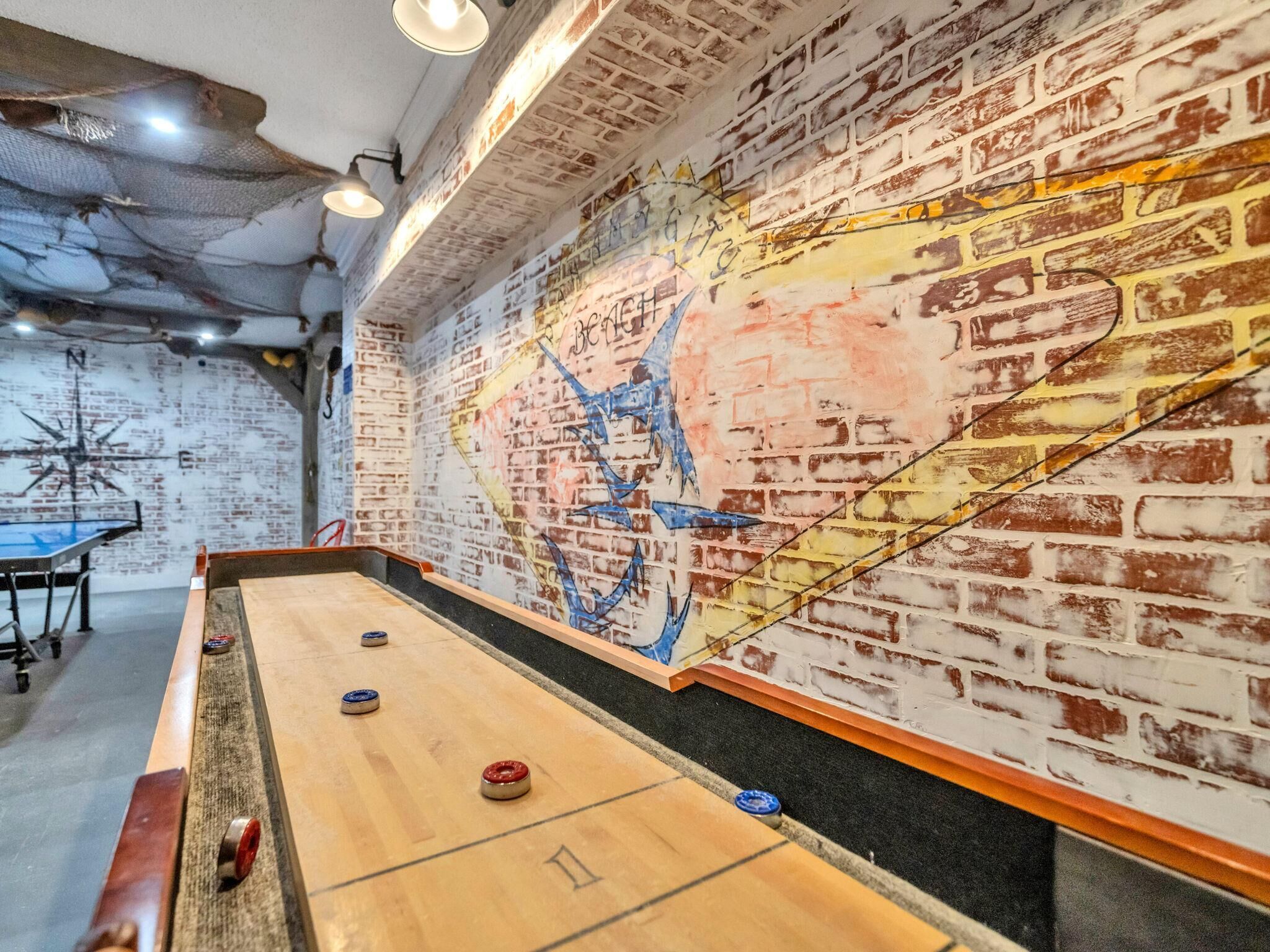 A shuffleboard table with pucks, a wall with a mural, and a brick wall.
