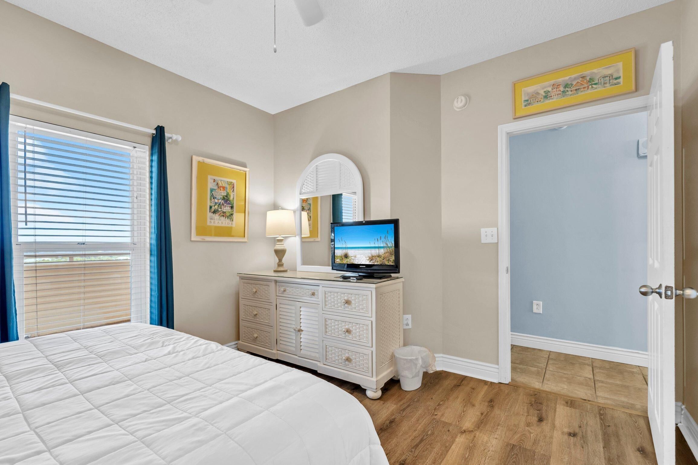 A bedroom with a bed, dresser, television, and a door.