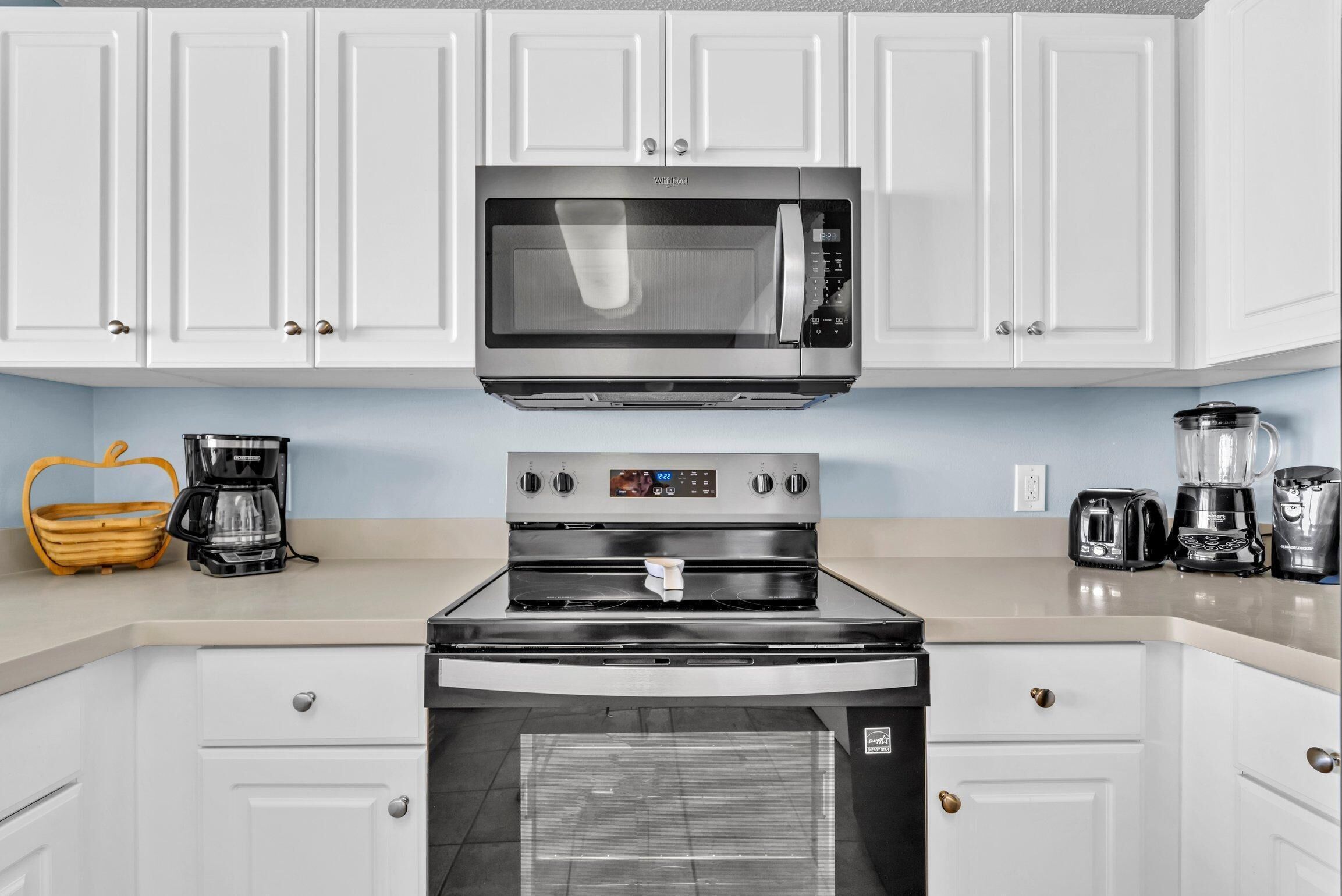 A modern kitchen with white cabinets, a stainless steel microwave, a built-in oven, and a coffee maker.