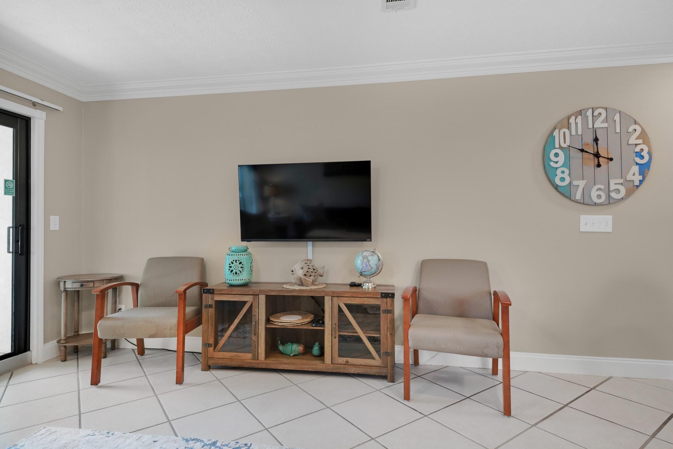 A living room with a TV, two chairs, a wooden cabinet, and a clock on the wall.