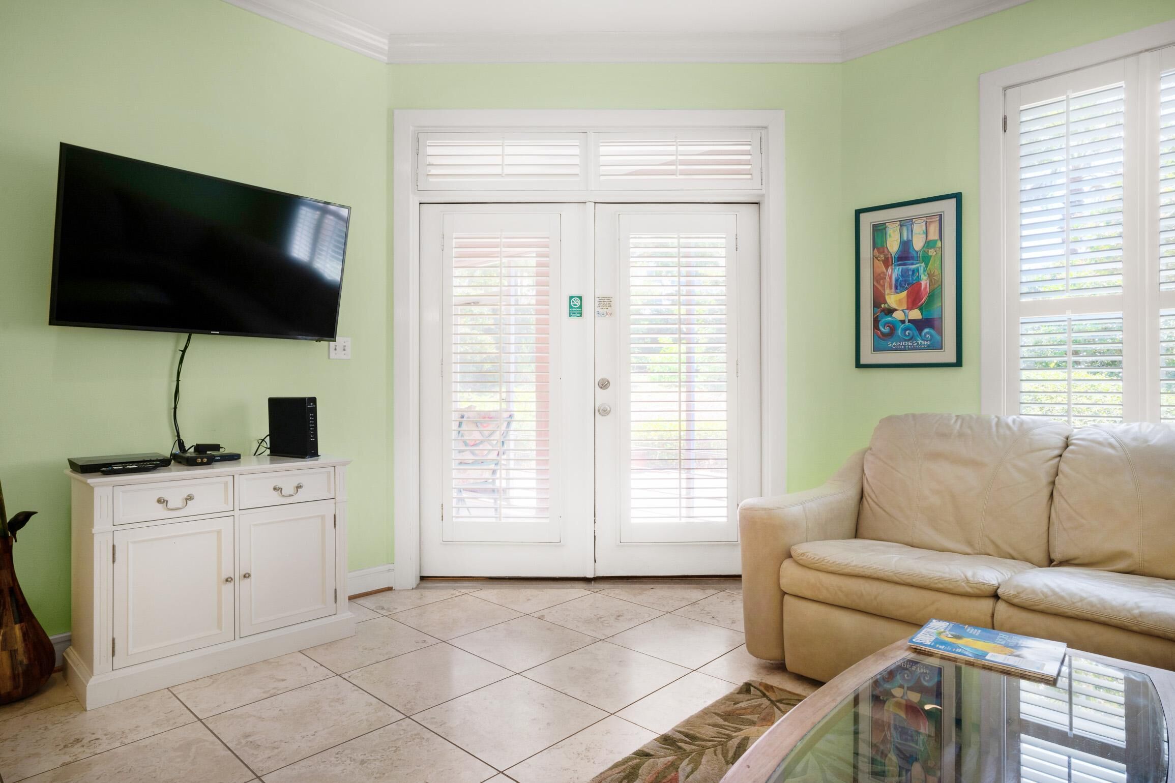 A living room with a flat-screen TV, a white cabinet, a beige sofa, and a glass coffee table.