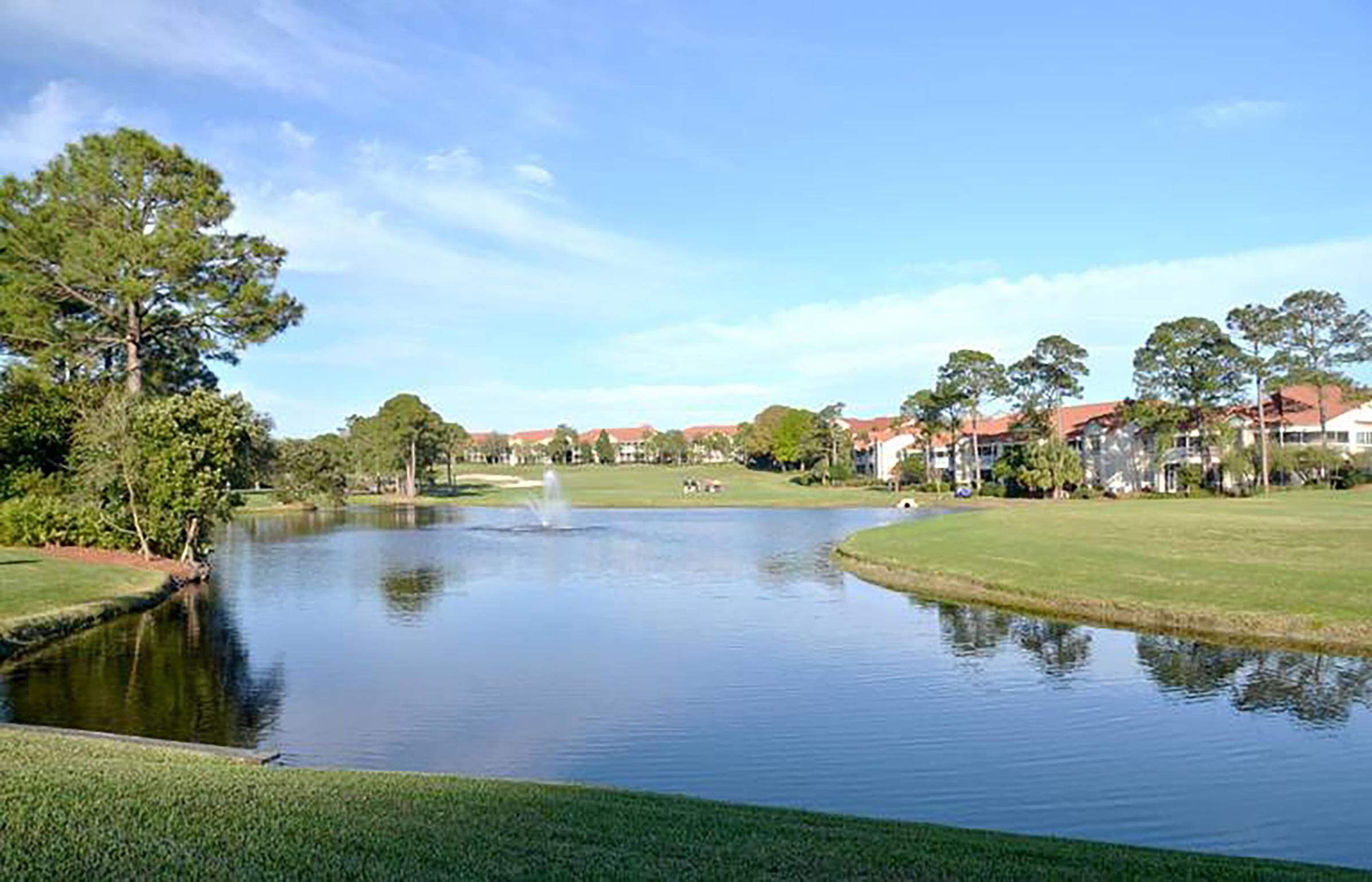 Ein Golfplatz mit Teich, Häusern im Hintergrund und blauem Himmel.