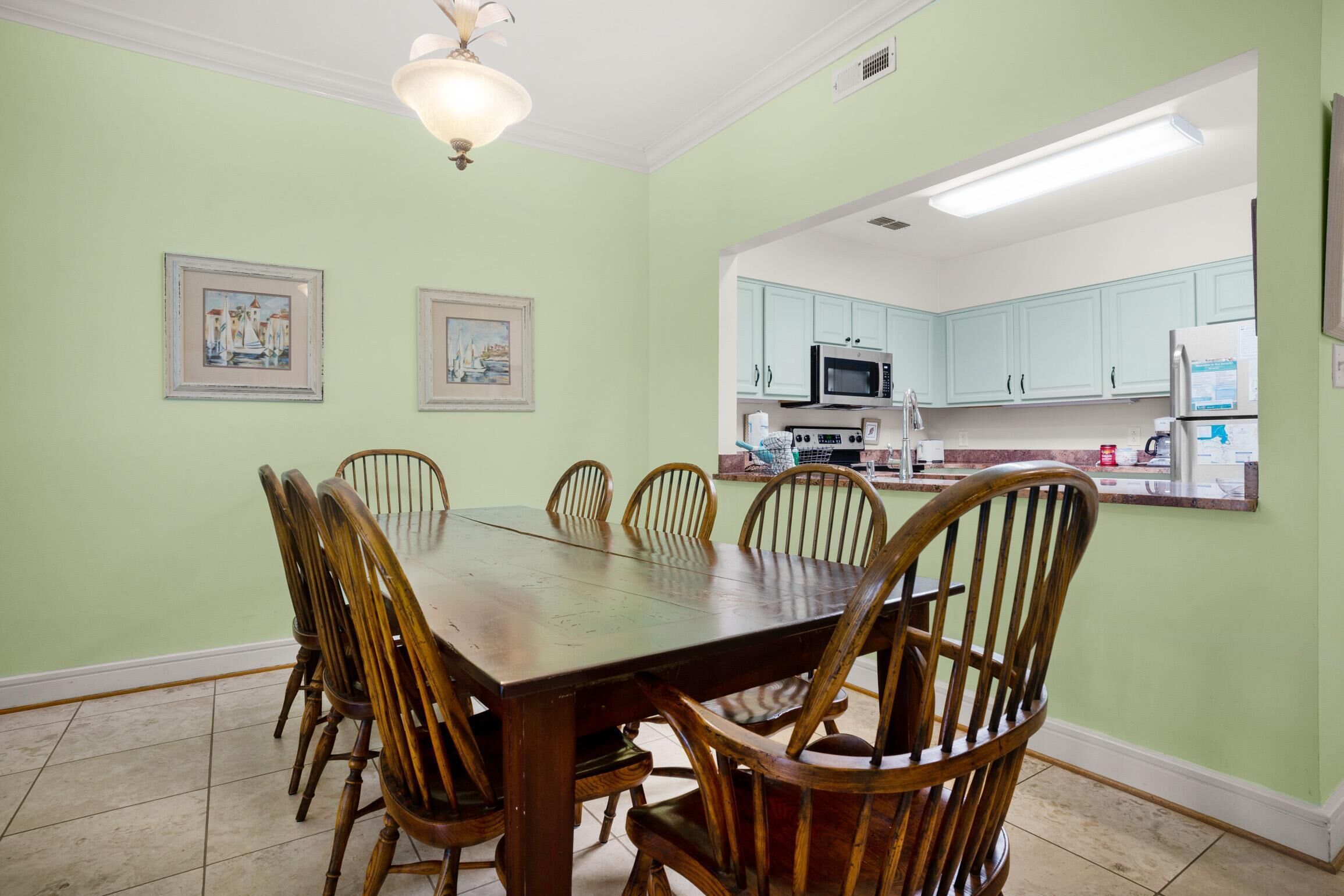 A dining area with a wooden table and chairs, a kitchen with light blue cabinets, and framed artwork on the walls.