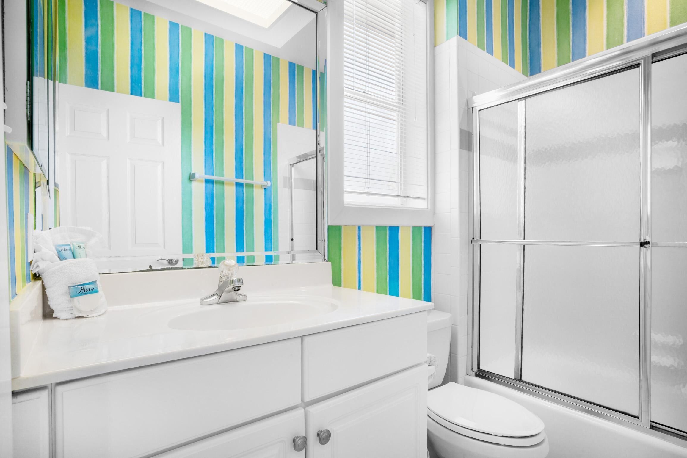 A bathroom with a striped wall, a white sink, and a glass shower enclosure.