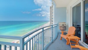 Un balcon avec vue sur une plage et l’océan, un barbecue et deux fauteuils Adirondack.